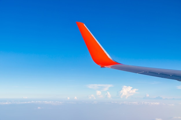 Roter Flügel des Flugzeuges mit Wolke und Bluesky vom Fenster