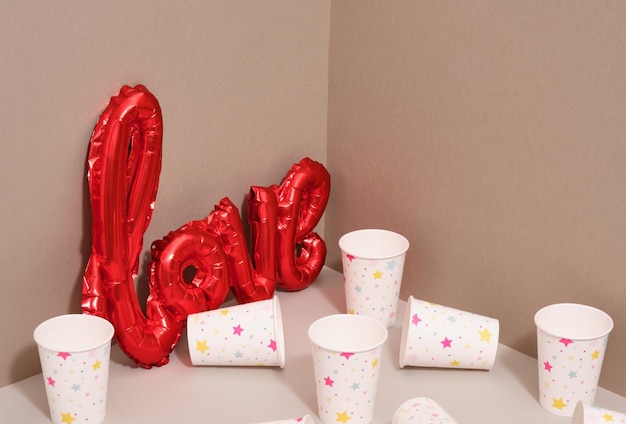 Roter Folienballon in Form des Wortes Liebe und viele schöne Tassen für Getränke auf dem Tisch