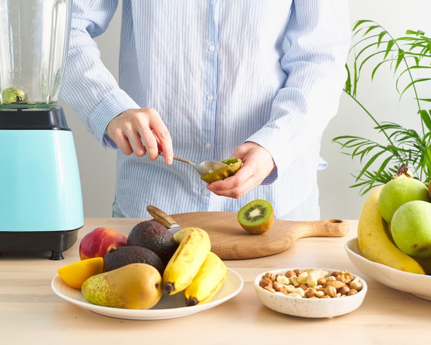 Roter Foodism grüner Smoothie mit Gemüse- und Obstfrau, die Kiwi zum Mixer Dash Diät schneidet