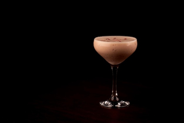 roter Fruchtsirup mit Löffel in einem Glas cremiger Baileys Milchlikör Cocktail auf einem Holztisch und dunkler Hintergrund allein