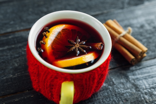 Roter gestrickter Becher Glühwein auf einem dunklen Holztisch