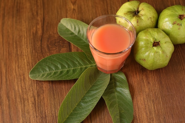 Roter Guavensaft wird auf einem hölzernen Hintergrund mit Guavenfruchtscheiben und Blattdekorationen serviert