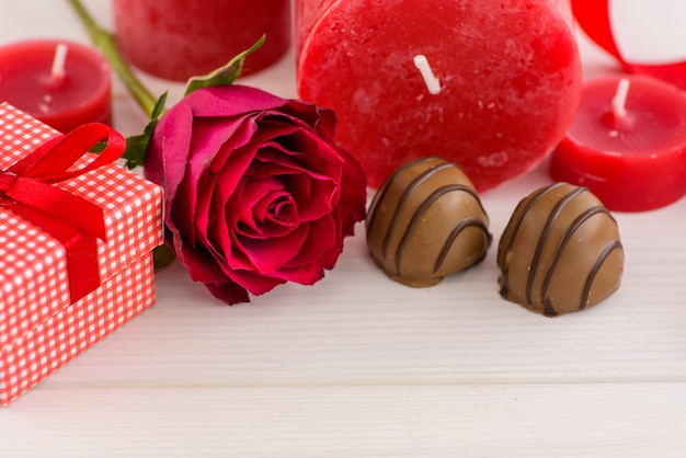 Roter Hintergrund des Valentinsgrußtages mit roten Rosen und Schokolade auf einem weißen Holztisch.