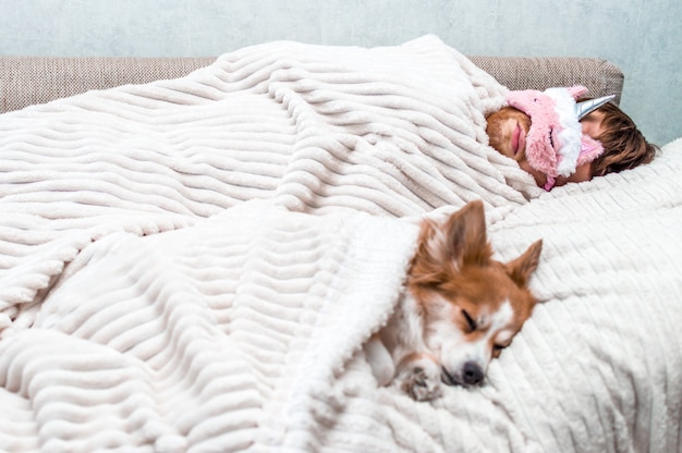 Roter Hund schläft mit seinem Besitzer in einer rosa Schlafmaske im Bett. Konzeptwochenende und Ruhe