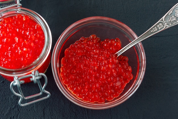 Roter Kaviar im Glasgefäß mit silbernem Löffel. Meeresfrüchte. Gesundes Essen. Diät. schwarzer Hintergrund.