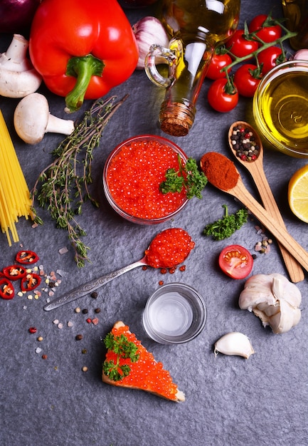 Roter Kaviar mit Gewürzen und Gemüse und mehr Essen auf schwarzem strukturiertem Hintergrund