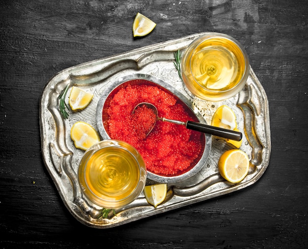 Roter Kaviar mit Weißwein auf dem alten Tablett. Auf einer schwarzen Tafel.