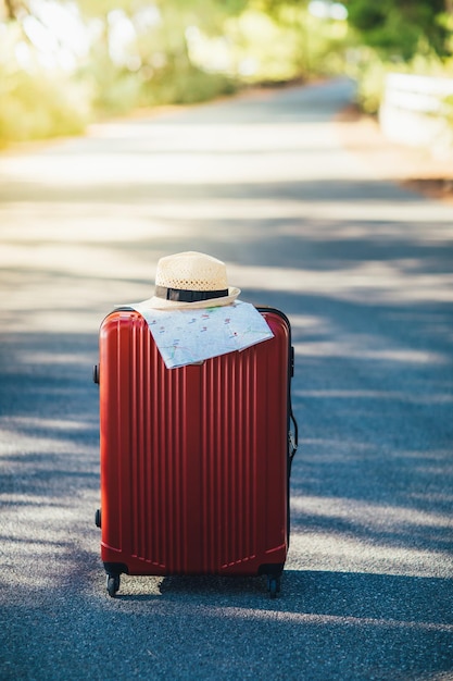 Roter Kofferhut und Karte auf der Straße auf dem Land Sommerurlaub und Reisekonzept