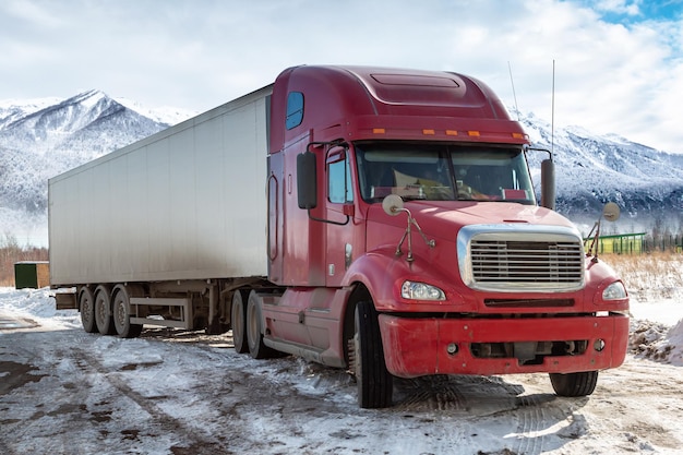 Roter Langstrecken-LKW mit Sattelanhänger im Winter auf dem Hintergrund hoher malerischer Berge