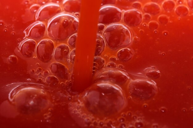 Roter Lebensmittelgeschäfthintergrund von Tomatensaft mit Spritzern und Blasennahaufnahme