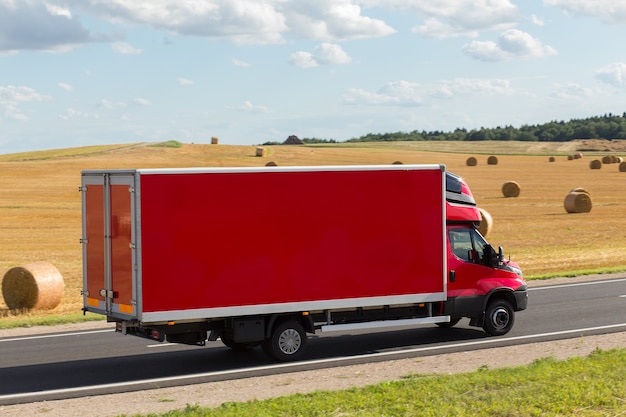 Roter Lieferweg, Lieferwagen auf der Autobahn, gegen ein gelbes geerntetes Weizenfeld. Es gibt einen Platz für Werbung