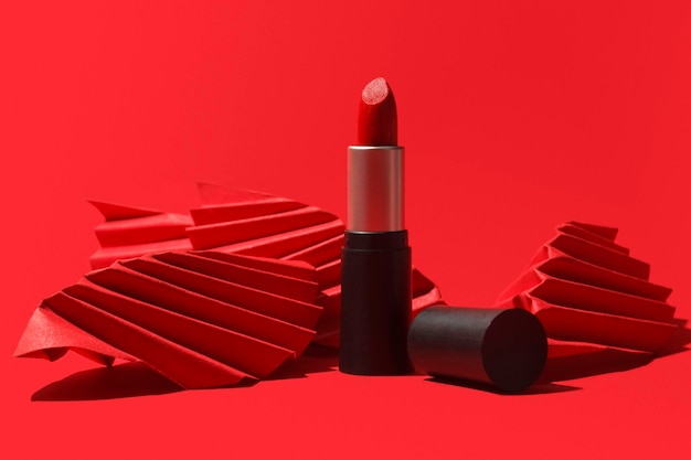 Roter Lippenstift mit Papierhandwerk auf rotem Grund. Kreatives Konzeptfoto von Kosmetik mit hartem Schatten