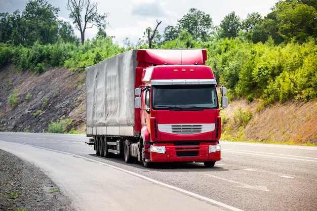 Roter LKW, der mit etwas Fracht durch eine Straße fährt