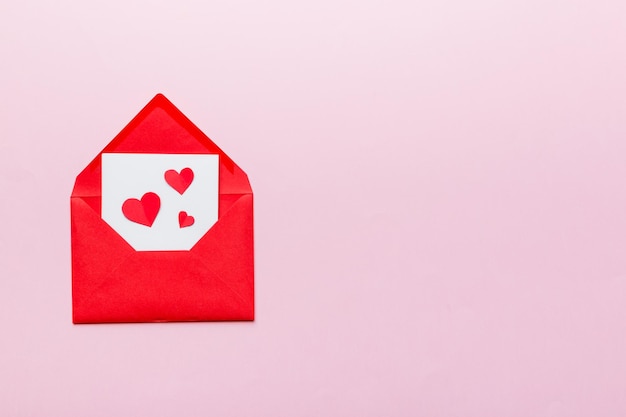 Roter Papierumschlag mit leerer weißer Karte und Herzen auf Draufsicht-Valentinstagkonzept des farbigen Hintergrundes