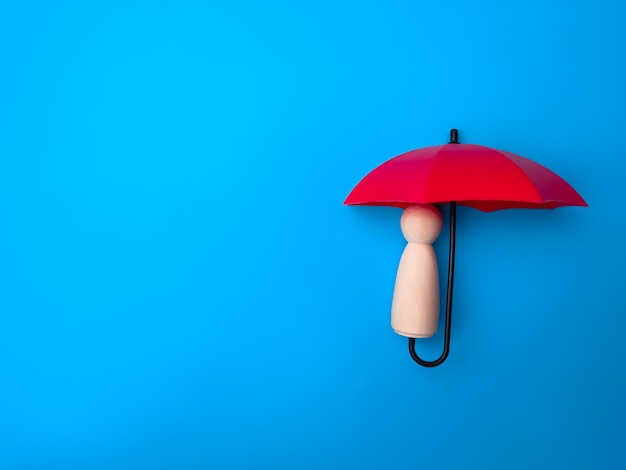 Roter Regenschirm mit Holzpflockpuppe auf blauem Hintergrund mit Kopierraum Schutzkonzept