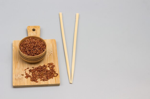 Roter Reis in einer Holzschale auf Schneidebrett. Bambusstöcke. Speicherplatz kopieren. Grauer Hintergrund. Draufsicht