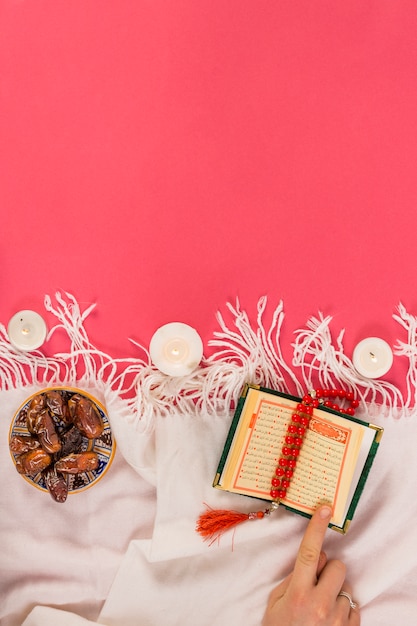 Foto roter rosenkranz; beleuchtung kerze; heiliges buch von koran und termine in der schüssel auf schal über rotem hintergrund