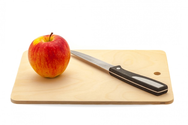 Roter saftiger Apfel und Messer auf einem Schneidebrett aus hellem Holz.