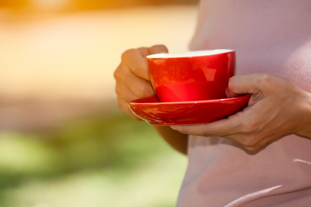 Roter Schalenkaffeesatz an Hand, der am Morgen auf unscharfem Grün hält