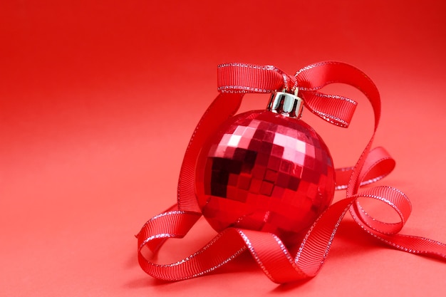 Roter Spielzeugball auf einem Weihnachtsbaum mit einem roten Band auf Rot
