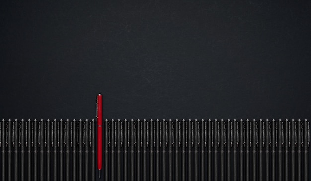 Roter Stift, der sich von der Reihe des schwarzen Stiftes abhebt. Flache Lage und Draufsicht mit Kopienraum auf schwarzem Hintergrund.