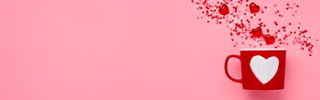 Foto roter tassenbecher mit gemalten herzen, zucker- und schokoladenherzen auf rosa hintergrund. flache zusammensetzung. valentinstag-konzept. ansicht von oben, kopienraum.