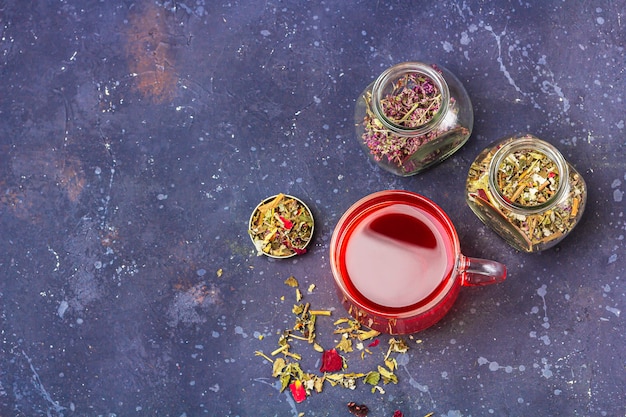 Roter Tee (Rooibos, Hibiskus, Karkade) in der Glasschale und in den Gläsern des trockenen Teeblatts und der Blütenblätter auf dunklem Hintergrund