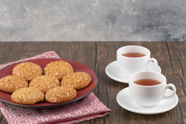 Roter Teller mit Haferkeksen und Tasse Tee auf Holztisch