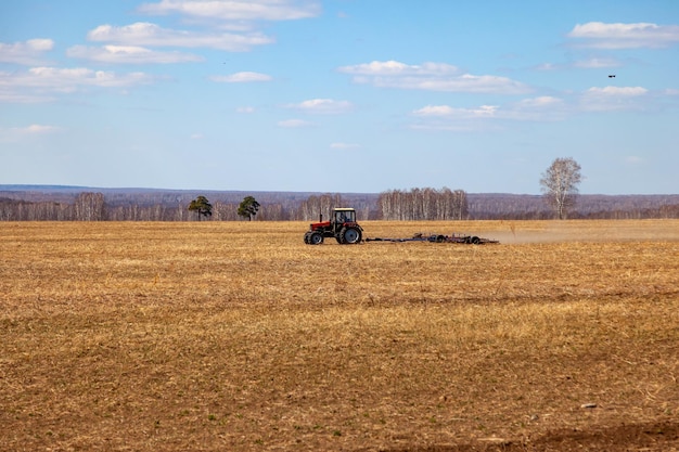 Roter Traktor mit gezogenem Pflug zum Mähen und Jäten von Feldern für die Agrarindustrie in Gelb