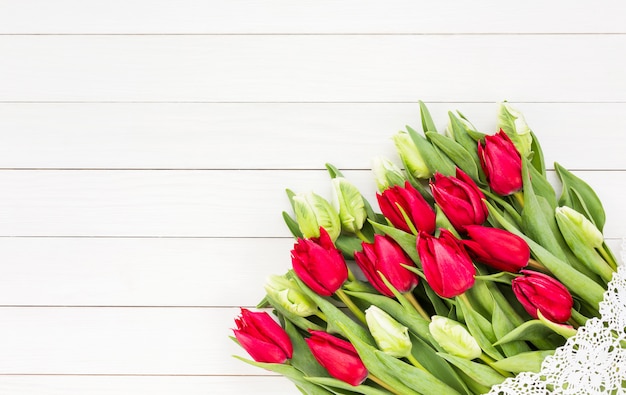 Roter Tulpenblumenstrauß verziert mit Spitze auf weißem Holztisch.