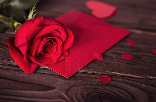 Roter Umschlag der Valentinstag-Geschenkkarte und rote Rose auf hölzernem braunem Hintergrund