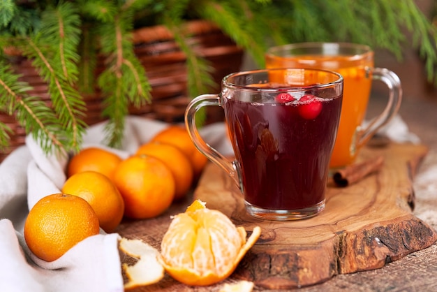 Roter und gelber Glühwein in Glasbechern auf einem Weihnachtstisch mit Mandarinen. Neujahrsstillleben hautnah