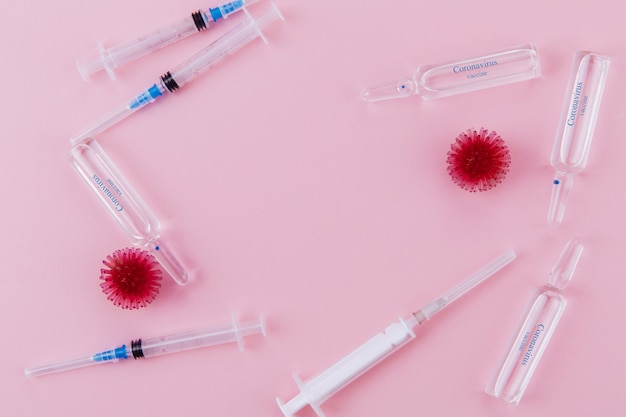 Roter Virus, Spritze und Ampullen mit Medizin auf einem rosa Hintergrund.
