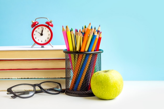 Roter Wecker, Apfel, Farbstifte, Bücher auf Blau