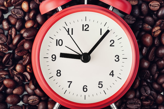 Roter Wecker, der auf Kaffeebohnen liegt. Sieben Minuten nach neun Uhr. Konzept des morgendlichen Erwachens, Beginn des Arbeitstages
