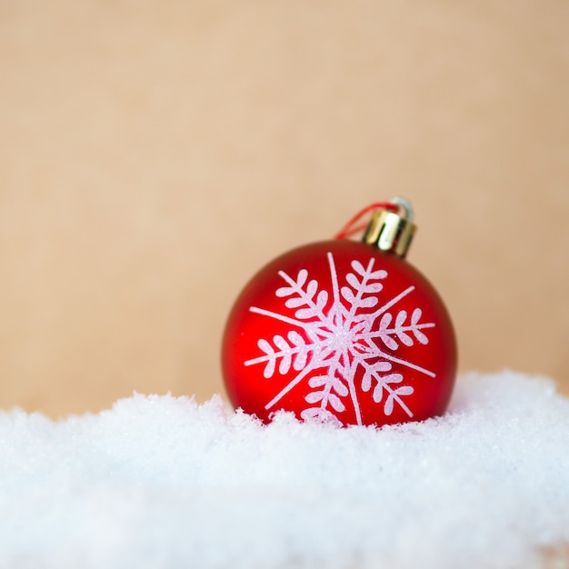 Roter Weihnachtsball mit einer gezeichneten Schneeflocke auf einer Schneewehe auf einem Handwerkshintergrund.