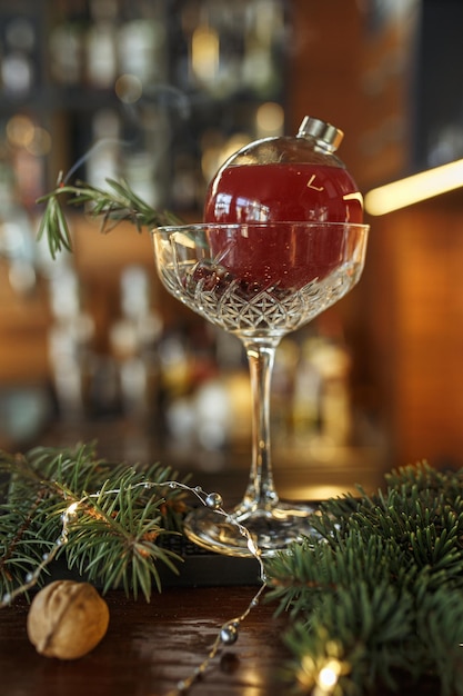 Roter Weihnachtscocktail in Glaskugel mit Rosmarinzweig, serviert auf der Theke in der Bar