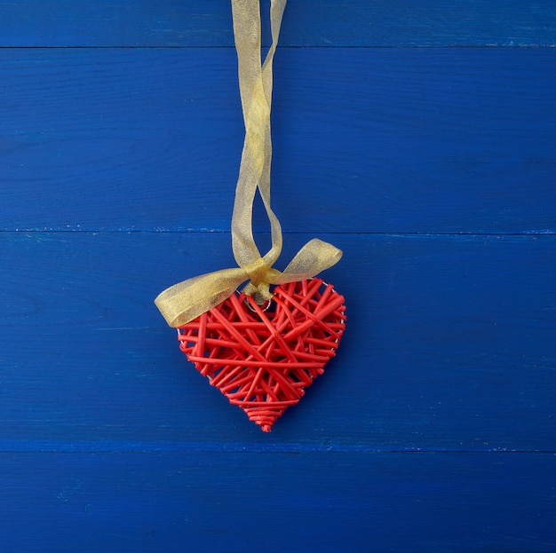 Rotes aus Weiden geflochtenes dekoratives Herz, das am silk goldenen Band hängt