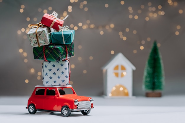 Rotes Auto mit Geschenken auf dem Dach. Vor dem Hintergrund des Hauses und des Baumes. Konzept zum Thema Weihnachten und Neujahr.