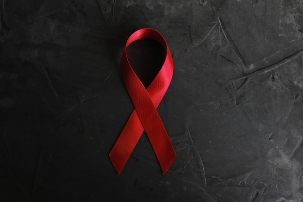 Rotes Band auf konkretem Beschaffenheitshintergrund, Symbol der AIDS-Krankheit und des Drogenmissbrauchsproblems.