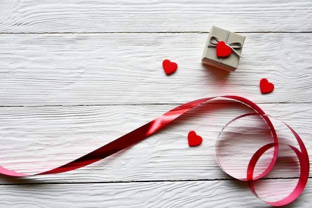 Rotes Band, kleine rote Holzherzen und Geschenkbox auf einem weißen Schreibtisch. Valentinstag Konzept