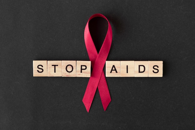 Rotes Band. Konzept für den Welt-AIDS-Tag. schwarzer Hintergrund, Kopienraum. Worte stoppen AIDS. Baner