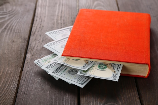 Rotes Buch mit verschachtelten Dollarbanknoten auf Holztisch Geldhaufen