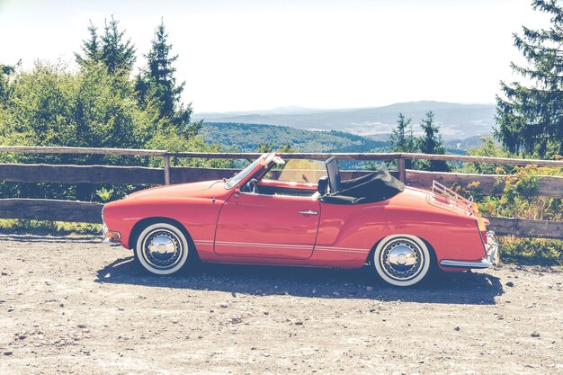 Rotes Cabriolet Coupe geparkt in der Nähe eines hölzernen Zauns mit Blick auf Bäume Foto