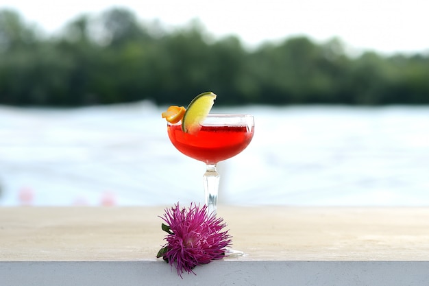 Rotes Cocktail in einem Becherglas mit einer Limettenscheibe. Mit Blumendekor