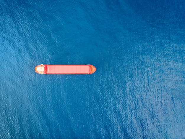 Rotes Containerschiff auf See von oben geschossen. Malerische Wasserlandschaft und einsames Boot, das im Export- und Importgeschäft und in der Logistik tätig ist. Fracht versenden. Wassertransport. Luftaufnahme des Meeres und des Bootes