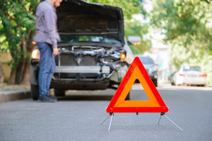 Rotes Dreieck Warnzeichen für Autounfall auf der Straße. Dreieck vor Autowrack und Fahrermann. Verletzter Mann bei Unfall schaut nach einem Unfall unter die Motorhaube des Autowracks.