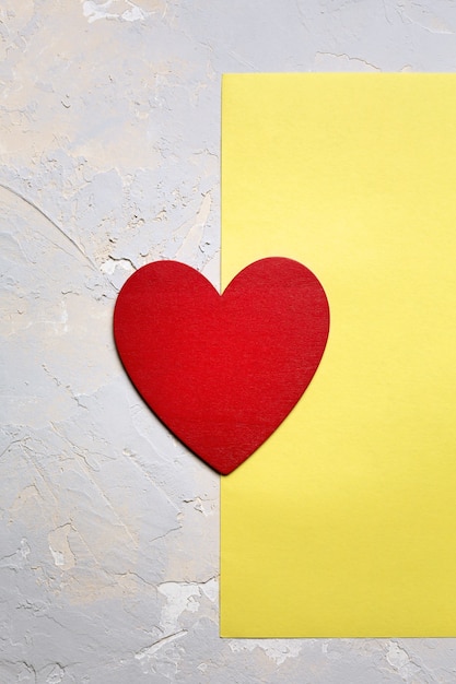 Rotes gemaltes Herz auf gelbem Papier auf grauem strukturiertem Hintergrund, minimalistische Karte des Valentinstags in der Pantone 2021-Farbe des Jahres