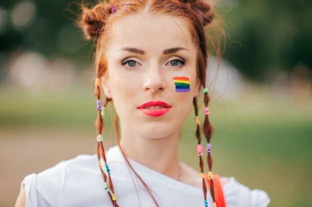 Rotes Haarmädchen mit lgbt schwulem Stolzflagge auf ihrem Gesichtsnahaufnahmeporträt.