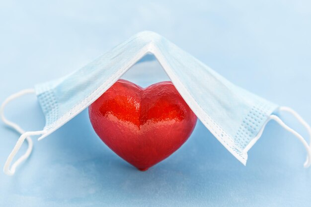 Rotes Herz, geschützt durch eine medizinische Maske auf blauem Hintergrund